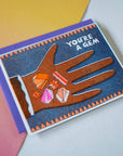 Greeting card with a hand holding gemstones and 'You're a Gem' text on a gradient background