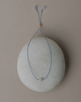 Blue string necklace with a small pendant on a gray stone surface