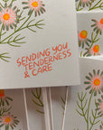 Card with floral design and text 'Sending you tenderness & care' on a matching background.