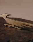 A small brass bird-shaped decorative object resting on a dark textured wooden surface against a soft beige background.