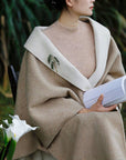 Person wearing a beige coat with a white flower and book in the foreground