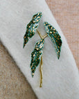 Green leaf-shaped brooch with gold accents on a fabric background