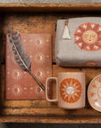 Decorative set with a mug, notebook, pouch, and dish featuring sun and moon designs on a wooden surface.