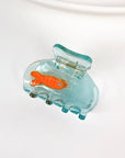 Add a little whimsy to your hairstyle with this mini koi fish claw clip. Made from smooth acetate with a sweet, sculptural silhouette, it brings a playful touch to half-ups, twists, and quick on-the-go styling. Lightweight, petite, and delightfully detailed, it’s an easy way to brighten your everyday look.