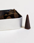 Incense cones in a metal box with one cone on a white surface