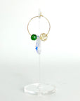Understated elegance with a twist. The Small Muse Hoops combine a soft champagne crystal and a rich emerald green stone to frame an asymmetrical feature crystal at the center. The result is a beautifully balanced mix of refinement and individuality—perfect for the quietly powerful.