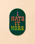 Sticker with 'I HATE IT HERE' text on a beige background