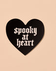 Black heart-shaped sign with 'spooky at heart' text on a beige background