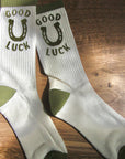 White socks with green accents and 'Good Luck' text on a wooden surface