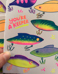 Card with colorful fishing lures and 'You're a Keeper' text