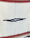 Close-up of a black and white diamond motif and red stripe on a cream woven blanket