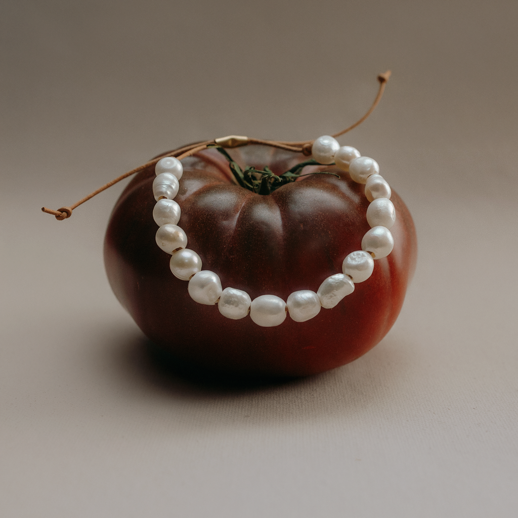 White freshwater pearl bracelet on a leather cord draped over a dark red tomato
