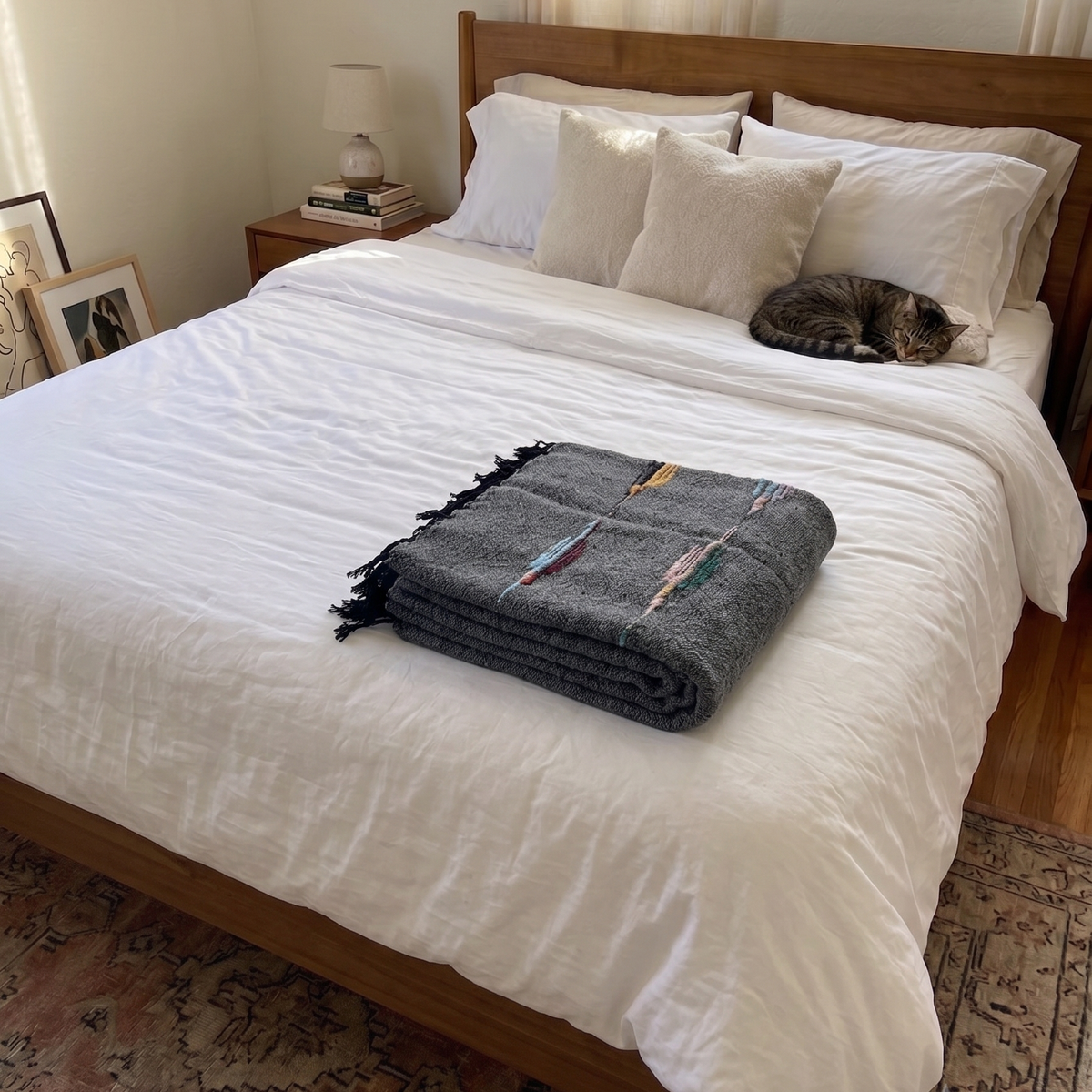 Folded charcoal wool thunderbird blanket on a white bed with a cat curled up near the pillows