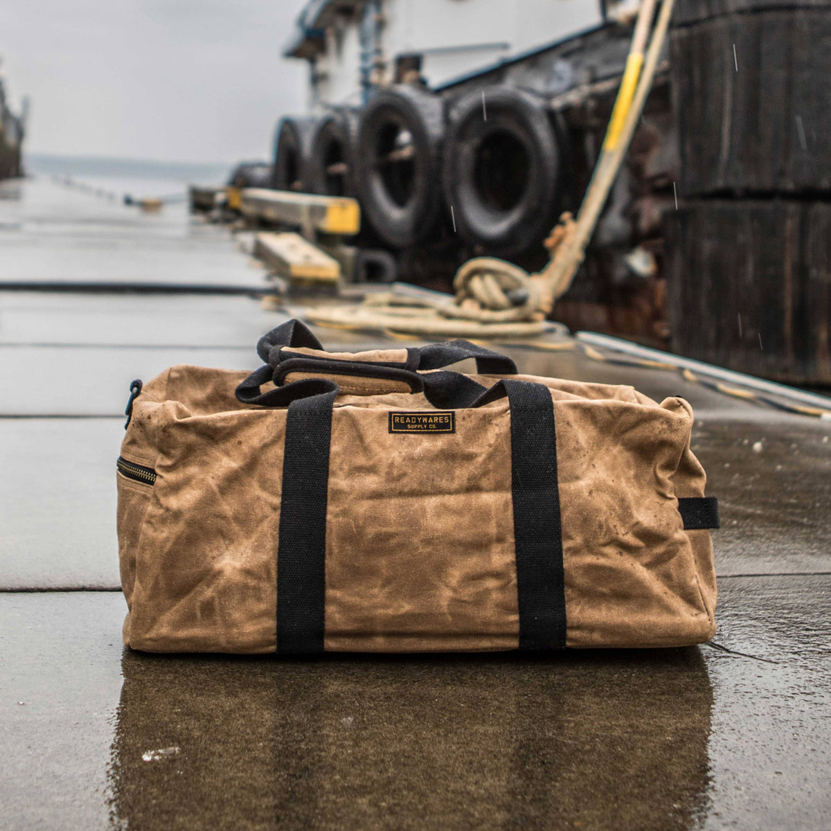 Waxed canvas duffel bag with webbing straps, padded handle and brass zipper