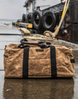 Waxed canvas duffel bag with webbing straps, padded handle and brass zipper