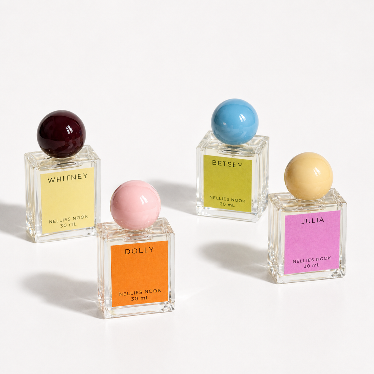 Whitney, Dolly, Betsey and Julia perfume bottles with colored sphere caps on a white background