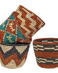 Three handwoven baskets in rust, teal and black patterns stacked and side by side on a white background