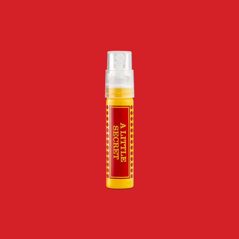 Yellow A Little Secret travel spray with a red label, on a red background