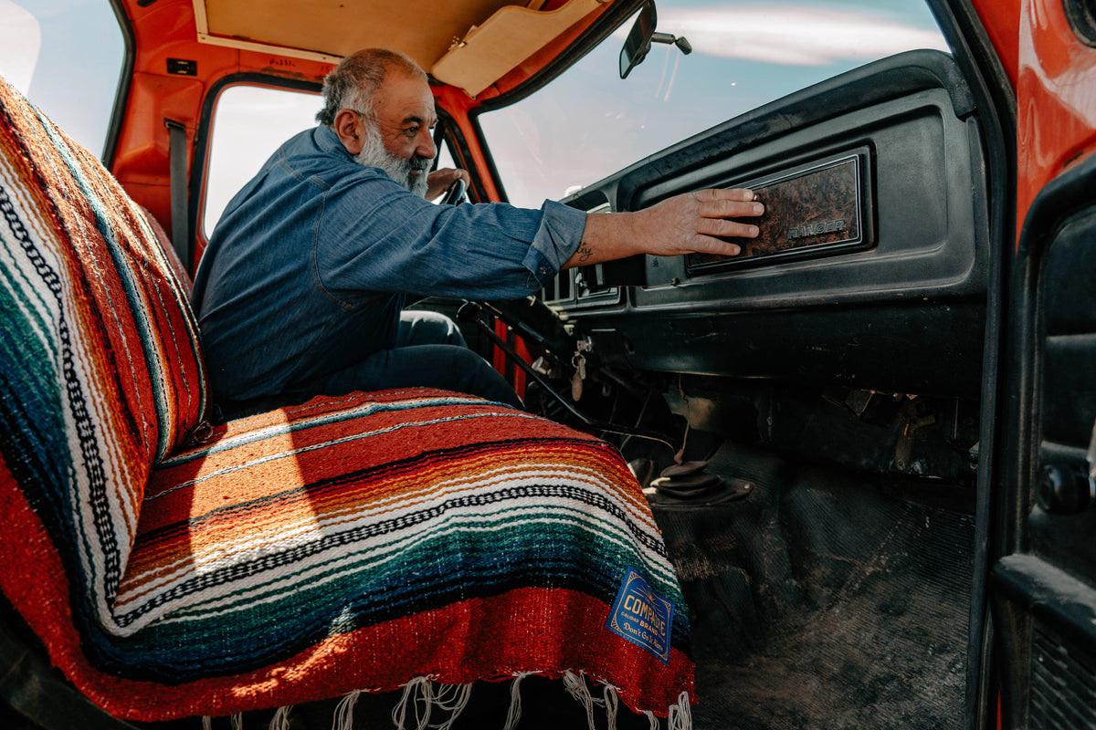 Man in a vintage truck cab with a red striped sarape across the seat