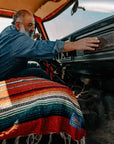 Man in a vintage truck cab with a red striped sarape across the seat