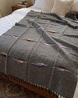 Charcoal wool thunderbird blanket spread on a bed with a cat sleeping on the pillow