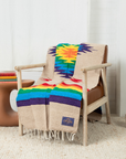Cream blanket with a colorful Southwest star and rainbow stripes draped over a wooden armchair