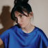 Woman with a top knot in a cobalt blue top wearing a small glass pendant necklace