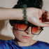 Woman in sunglasses resting a wrist wearing a green glass bubble bracelet on her brow