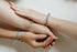 Two clasped hands wearing blue and green beaded bracelets