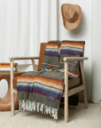 Olive green striped sarape draped over a wooden armchair with a straw cowboy hat on the wall