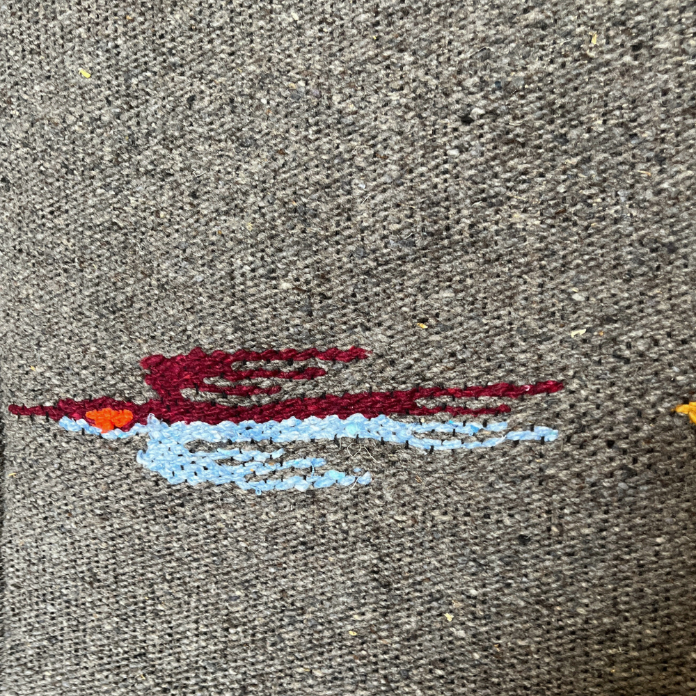 Close-up of a red and light blue thunderbird woven into charcoal wool