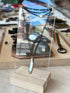 Mini folding knife pendant with pearl inlay on a black chain, hanging on an acrylic stand