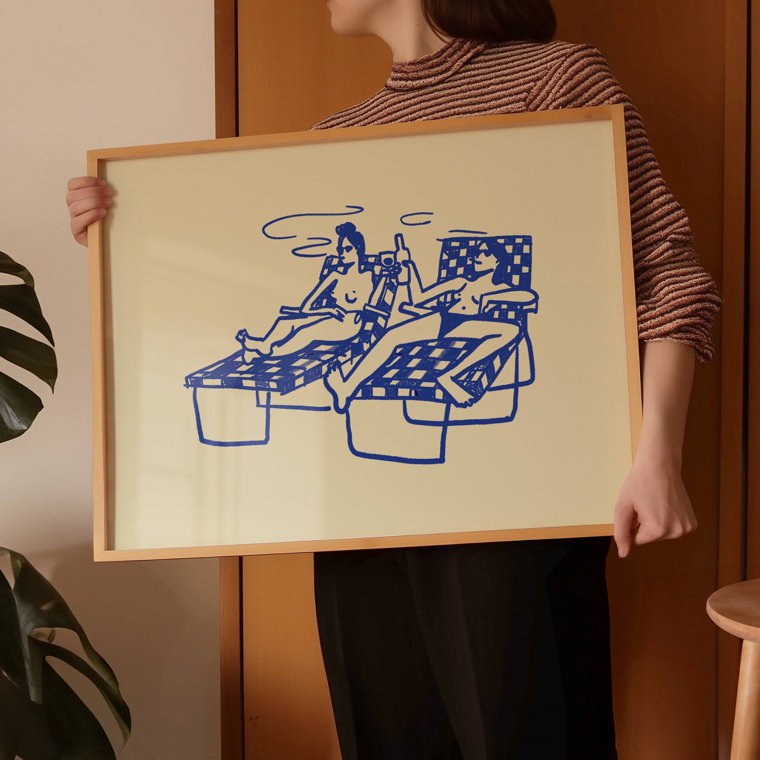 This piece of art feels like a mini-vacation. This unframed art print captures a delightful moment of two ladies basking in the sun by the pool, sipping cocktails and wine. With a soft butter yellow background and dark blue line drawing, it's a wonderfully relaxing piece of wall art that brings a touch of summer fun to any home decor collection.