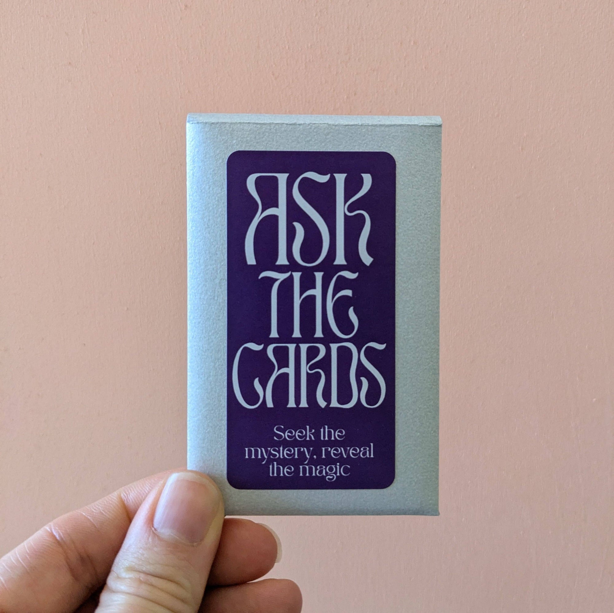 Card deck with 'Ask the Cards' text held by a hand against a pink background