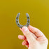Hand holding a small metal horseshoe against a mustard yellow background