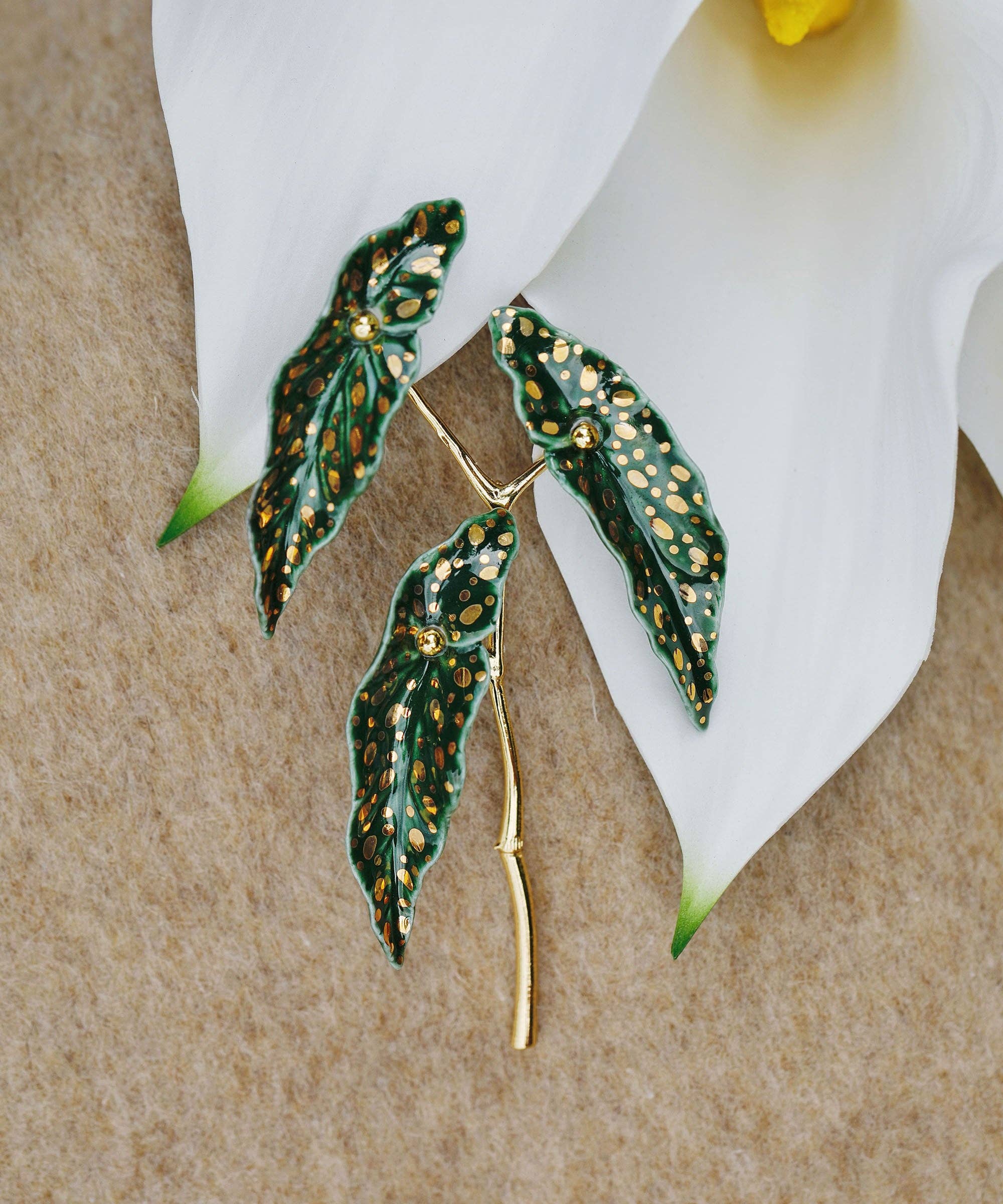Green leaf-shaped brooch with gold accents on a white flower background