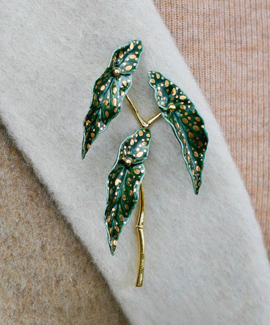 Green leaf-shaped brooch with gold accents on a fabric background