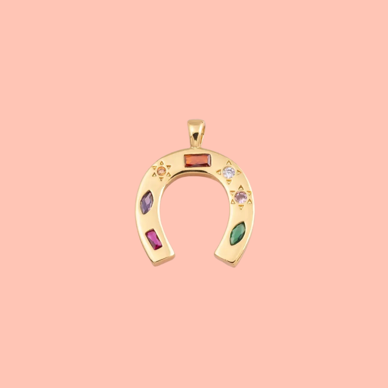 Gold horseshoe-shaped pendant with colorful stones on a pink background