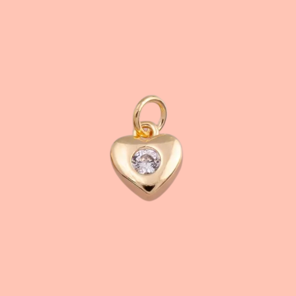 Gold heart-shaped pendant with a clear gemstone on a pink background