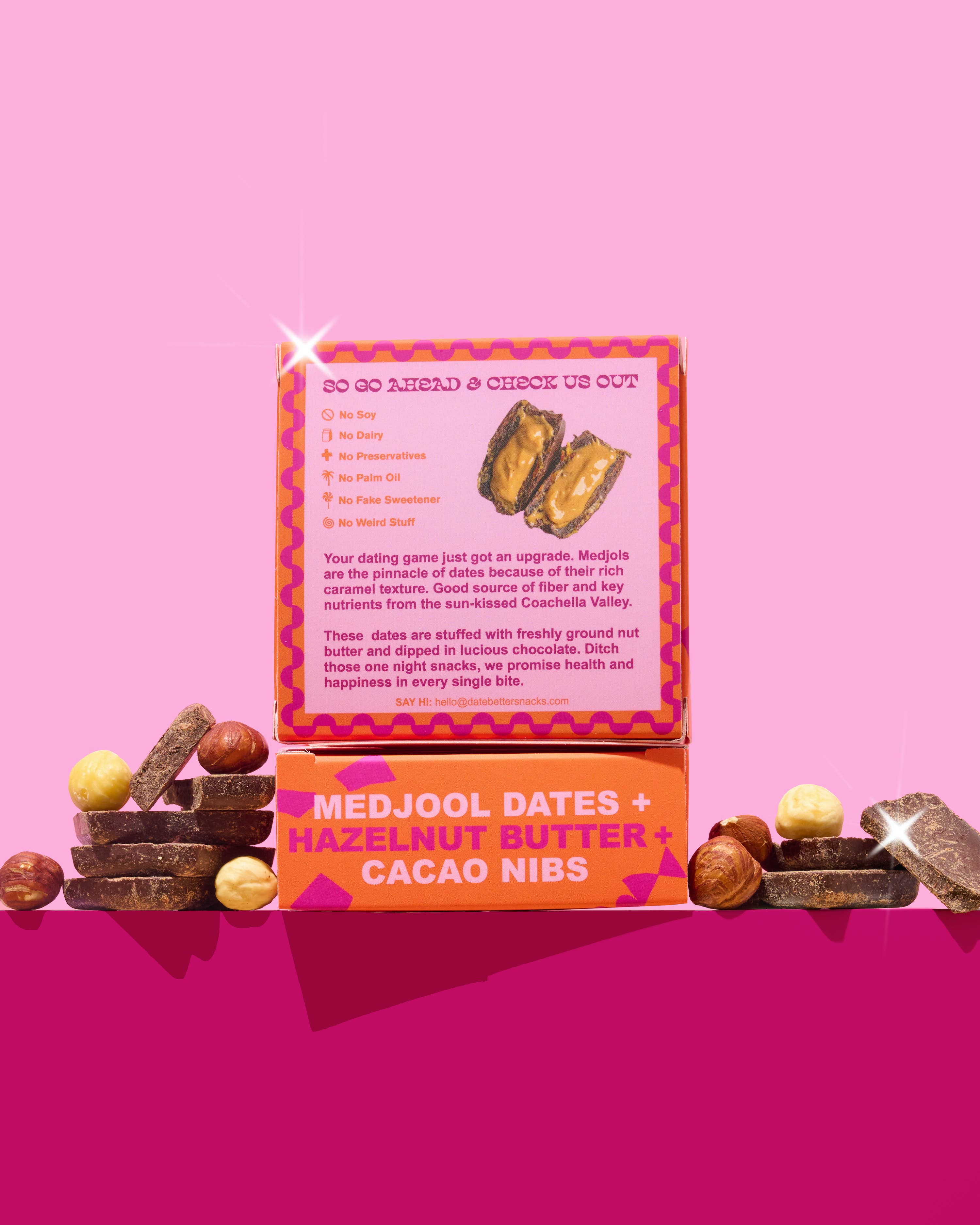 Box of Medjool dates, hazelnut butter, and cacao nibs on a pink background