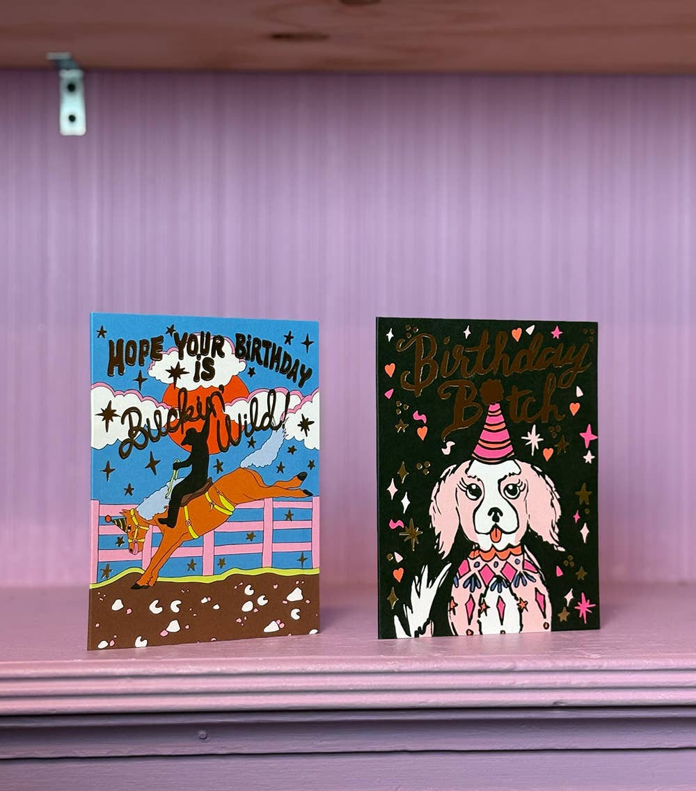 Two birthday cards on a purple surface with a pink curtain background.