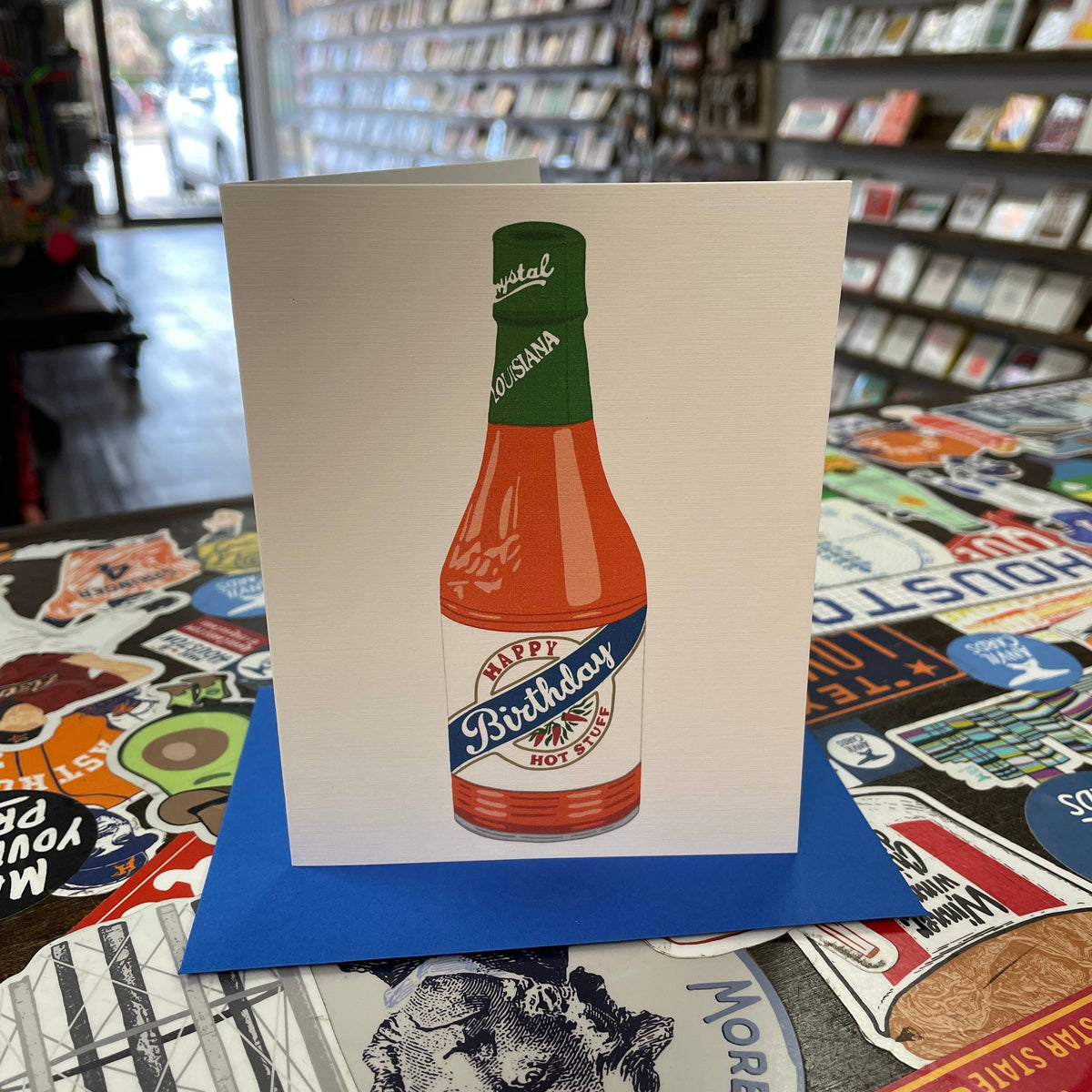 Spice up your birthday wishes with this Hot Stuff Crystal greeting card! Made in Houston, Texas, this card features a bottle of Crystal hot sauce with a quirky message and unique illustrated artwork. Blank inside, perfect for adding your own unique touch. Get saucy and celebrate!