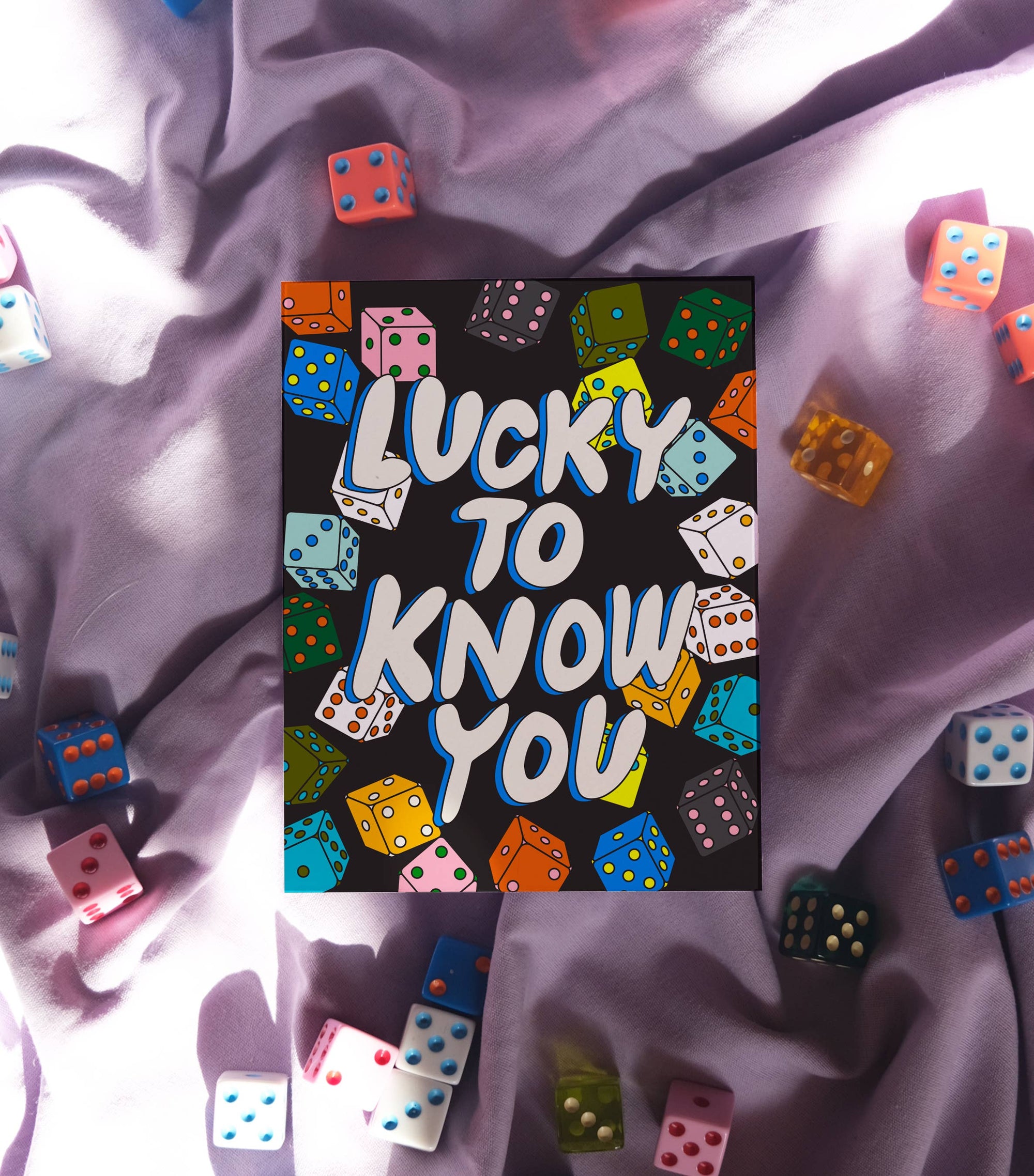 Card with 'Lucky to Know You' text surrounded by colorful dice on a textured surface