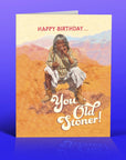 Birthday card with a person smoking and text 'Happy Birthday... You Old Stoner!' on a desert background.