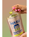Hand holding a packet of HARU Matcha Oat Milk Latte with a spoonful of matcha powder.