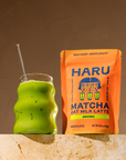Green matcha oat milk latte in a glass with a Haru Matcha oat milk latte package on a brown background