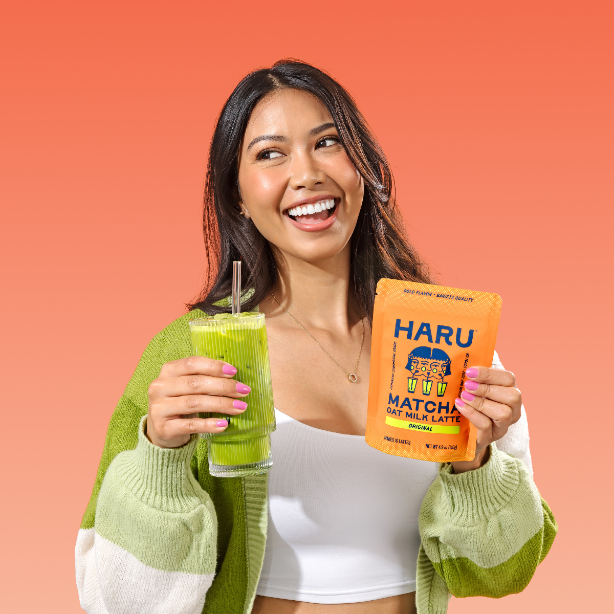 Woman holding a green smoothie and a Haru Matcha Latte package against an orange background