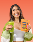 Woman holding a green smoothie and a Haru Matcha Latte package against an orange background