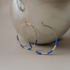 Gold hoops with a blue and white beaded pattern resting on a white ceramic piece