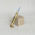 Brass sliding blade knife keychain with the blade extended, leaning on a wood block